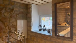A stone-walled room with a window, a white cabinet, and a metal rack with hooks.