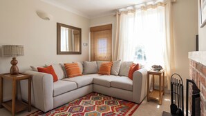 Una sala de estar con un sofá modular, una alfombra estampada, una lámpara y una chimenea.