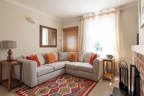 A living room with a sectional sofa, a patterned rug, a lamp, and a fireplace. - A quaint cottage located directly on Emsworth's Mill Pond, just steps into Emsworth town and waterfront. (Emsworth)