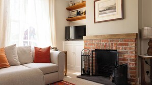 Una sala de estar con un sofá, chimenea, televisor y estantería.