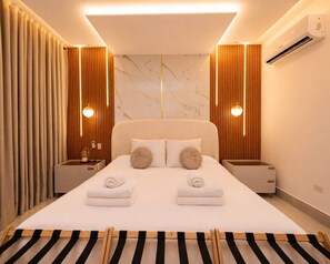 Une chambre d’hôtel moderne avec un grand lit, deux tables de chevet, un climatiseur fixé au mur et un tapis à rayures.