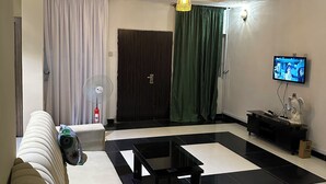 Una sala de estar con un sofá, una mesa de centro, un televisor y un ventilador.
