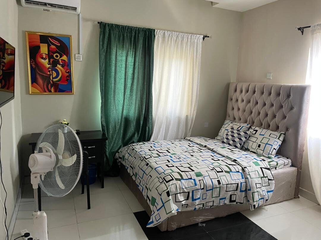 Un dormitorio con una cama, un ventilador, un escritorio y un cuadro en la pared.