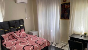 Un dormitorio con cama, escritorio, silla, aire acondicionado blanco y un cuadro en la pared.
