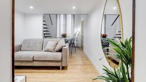 Ein modernes Wohnzimmer mit einer Couch, einem Esstisch und Stühlen. An der Wand befindet sich ein großer Spiegel und eine Treppe, die in eine weitere Ebene führt.