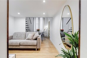 Ein modernes Wohnzimmer mit einer Couch, einem Esstisch und Stühlen. An der Wand befindet sich ein großer Spiegel und eine Treppe, die in eine weitere Ebene führt.