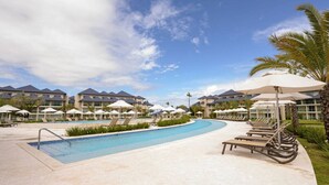 Ein Poolbereich eines Resorts mit Liegestühlen, Sonnenschirmen und Hotelgebäuden im Hintergrund.