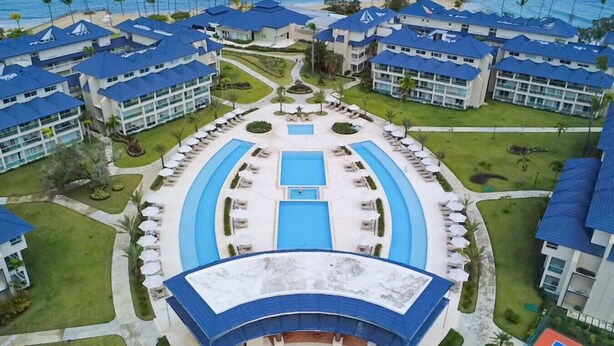 Ein Resort mit mehreren Gebäuden mit blauen Dächern, einem zentral gelegenen Schwimmbad und einem Tennisplatz.