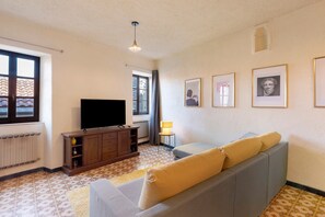 Una sala de estar con un sofá, televisión, un mueble y cuadros en la pared.
