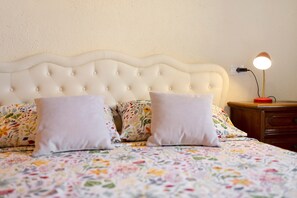 Una cama con una colcha de estampado floral, cabecera tapizada y dos almohadas blancas.