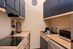 A compact kitchen with dark cabinets, a stainless steel oven, and a wall clock.