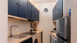 A compact kitchen with dark cabinets, a stainless steel refrigerator, a sink, and a clock on the wall.