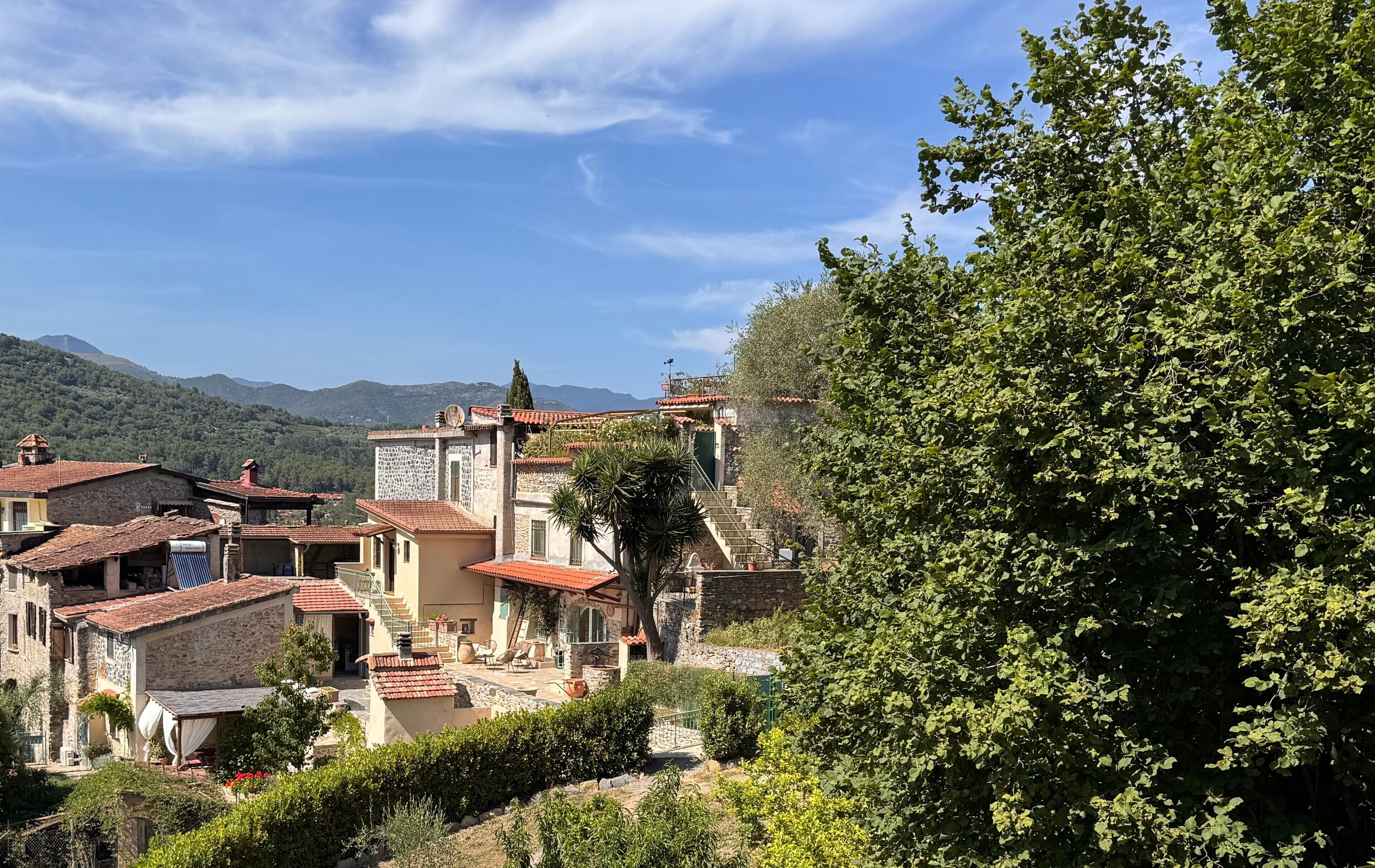 Ein Dorf an einem Hang mit traditionellen Steinhäusern, einer Treppe, die zu einer Terrasse führt, und üppiger Vegetation.