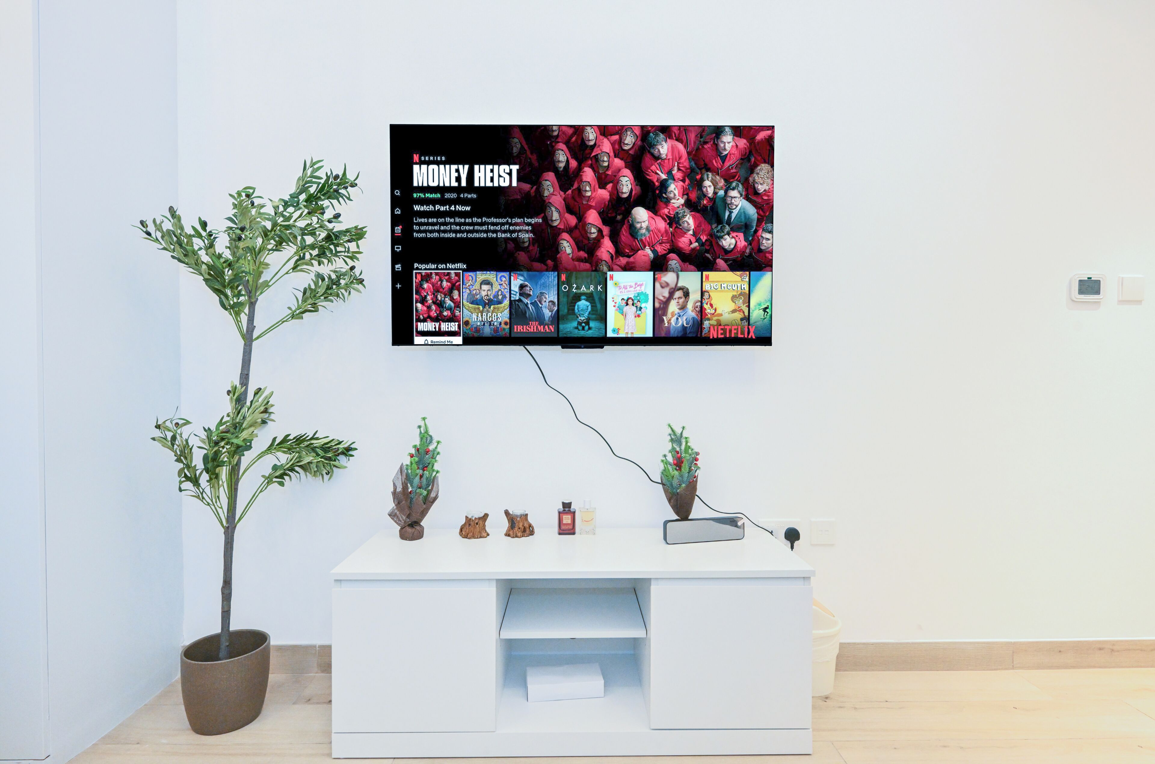 A modern room with a white reception desk, a potted plant, and a flat-screen TV displaying a Netflix show.