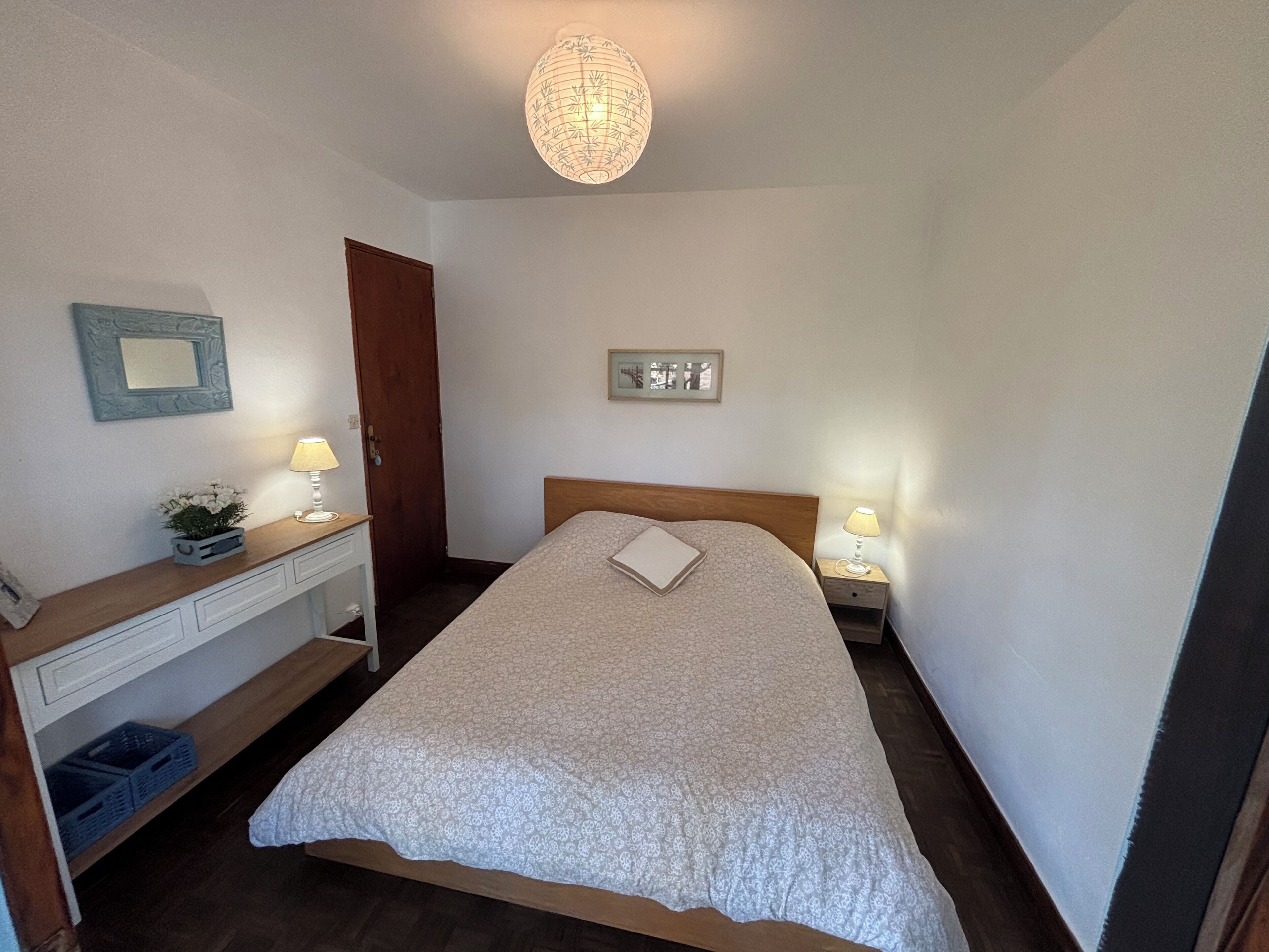 A bedroom with a bed, bedside lamps, a nightstand, a dresser, a mirror, and a hanging light fixture.