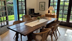 A dining area with a wooden table, wicker chairs, a potted plant, and a television. - Charming Villa in Cap-Ferret (Lège-Cap-Ferret)