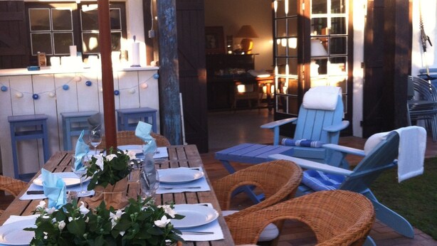 An outdoor dining area with a wooden table set for a meal, wicker chairs, and an umbrella providing shade. - Charming Villa in Cap-Ferret (Lège-Cap-Ferret)