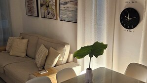 Olohuoneessa on lasinen ruokapöytä, sohva, viherkasvi ja seinäkellot, joissa näkyy eri kaupunkien aika.
