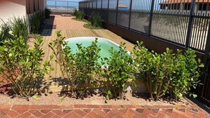 A pool area with a fenced patio, surrounded by plants and a clear view of the sea.