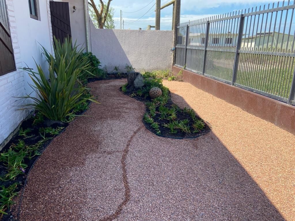 A paved pathway with plants and a fence.