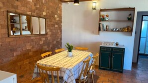 A dining area with a brick wall, wooden table, chairs, and a potted plant.