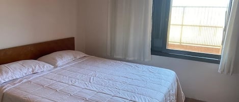 A single bed with a wooden headboard in a room with a window and curtains.