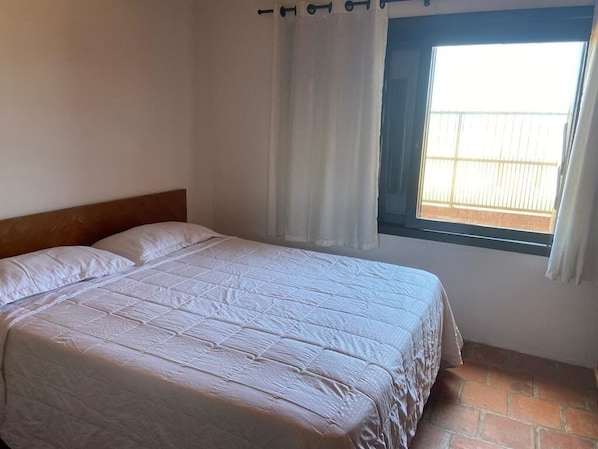 A single bed with a wooden headboard in a room with a window and curtains.