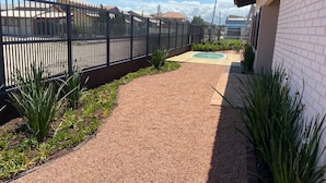 A pathway leading to a sports court, surrounded by a fence and plants.