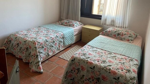 A bedroom with two beds, a window with curtains, and a tiled floor.