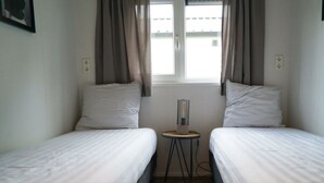 A small, clean room with two single beds, a small table, and a window with curtains. - Holiday Home in Kampen With Terrace (Kampen)