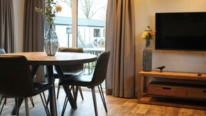 A modern living room with a dining table, chairs, a flat-screen TV, and a large window with curtains. - Holiday Home in Kampen With Terrace (Kampen)