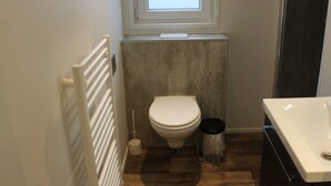 A small bathroom with a toilet, a radiator, a window, and a sink. - Holiday Home in Kampen With Terrace (Kampen)