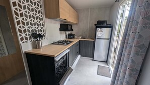 Eine kompakte Küche mit Kochinsel, Backofen, Kühlschrank und einem Fenster mit gemusterten Vorhängen.