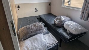 Ein kleines Zimmer mit zwei Betten, einem Fenster und einer kompakten Küchenzeile.