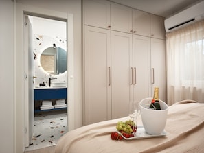 A hotel room with a bed, a bedside table with a bottle of champagne, a glass, and grapes. There is a bathroom visible through an open door. - Luxury Seafront Villa Kaprije Šibenik with pool (Kaprije)