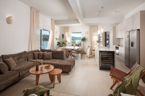 A modern living room with a sofa, coffee table, and chairs, a dining area with a table and chairs, and a kitchen with a refrigerator and cabinets. - Luxury Seafront Villa Kaprije Šibenik with pool (Kaprije)