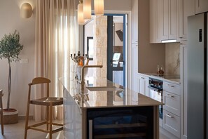 A modern kitchen with a marble countertop, stainless steel appliances, and a dining area with a wooden chair and table. - Luxury Seafront Villa Kaprije Šibenik with pool (Kaprije)