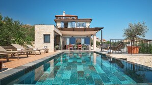 Una moderna casa a due piani con piscina, area salotto esterna e giardino.
