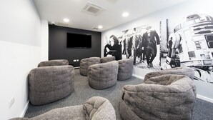 Una habitación con sillones tipo bean bag grises, un televisor de pantalla plana y un mural en la pared.