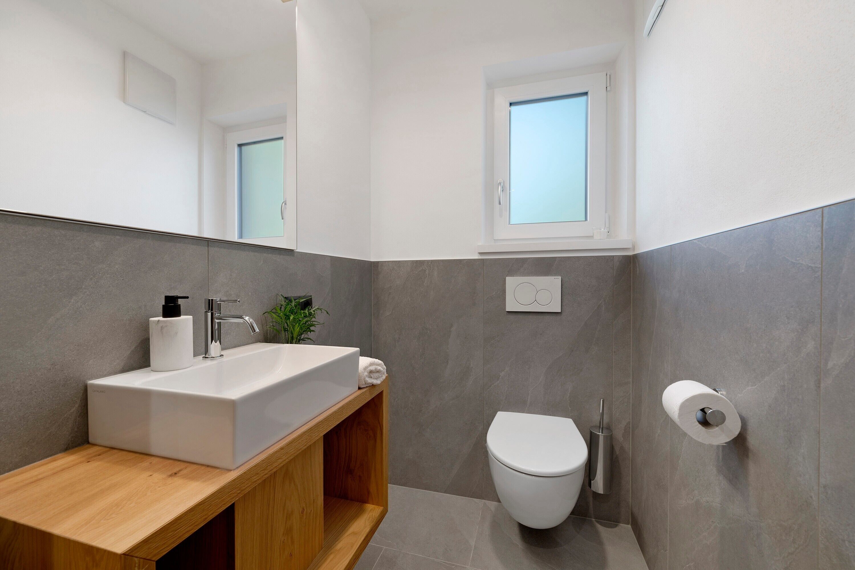 Une salle de bain moderne avec un grand miroir, un lavabo blanc, des toilettes et une fenêtre.