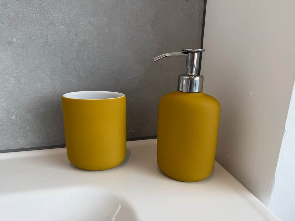 A bathroom with a white sink, a yellow soap dispenser, and a yellow cup.
