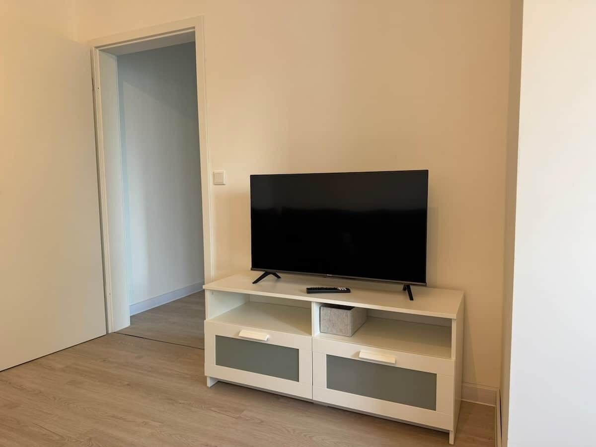 A white entertainment unit with a flat-screen TV, a remote, and storage drawers.