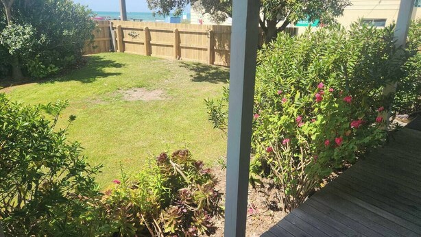 A backyard with a wooden deck, a grassy lawn, and various plants. - Esplanade Escape – Classic Coastal Cottage (Kaka Point)