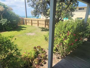 A backyard with a wooden deck, a grassy lawn, and various plants. - Esplanade Escape – Classic Coastal Cottage (Kaka Point)