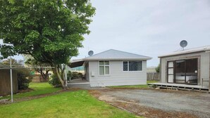 A single-story house with a covered porch, a satellite dish, and a well-maintained lawn. - Esplanade Escape – Classic Coastal Cottage (Kaka Point)