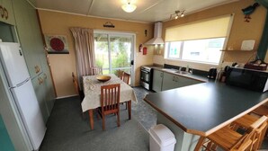 A compact kitchen with a dining table, chairs, a refrigerator, and a microwave. - Esplanade Escape – Classic Coastal Cottage (Kaka Point)
