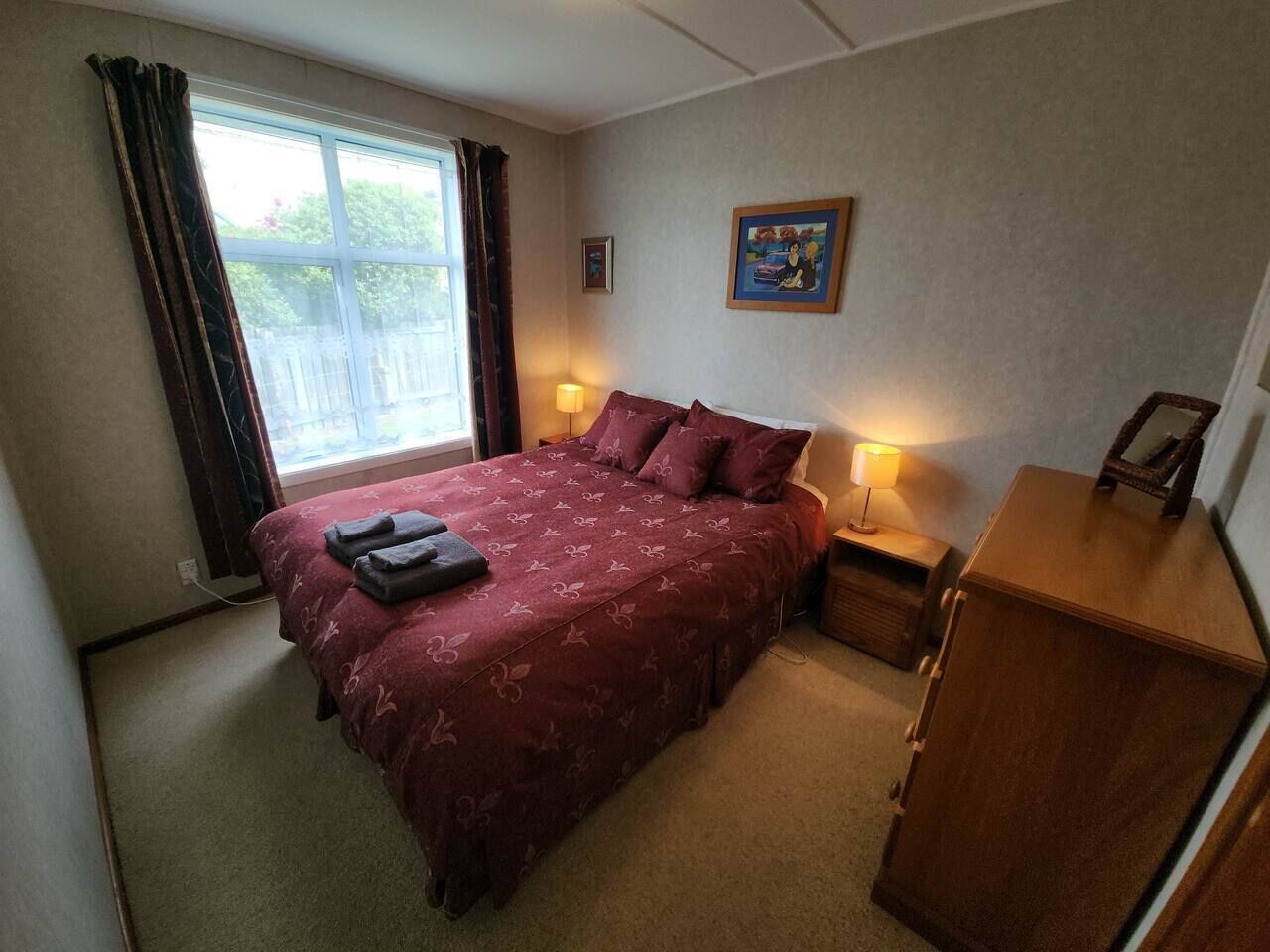 A bedroom with a bed, bedside lamps, a dresser, a window with curtains, and a painting on the wall.