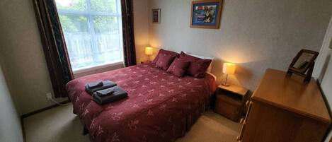 A bedroom with a bed, bedside lamps, a dresser, a window with curtains, and a painting on the wall.