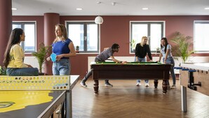 A pool table in a room with large windows, a foosball table, and potted plants. - Unite Students - Emily Bowes - London (London)