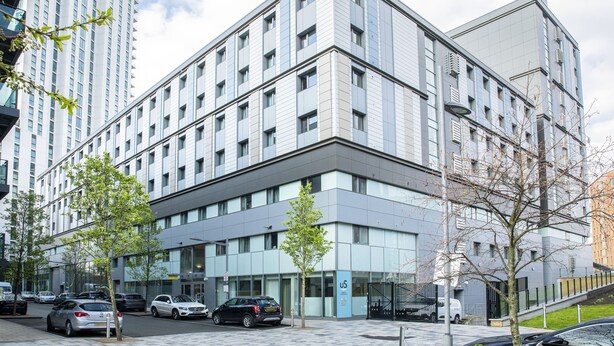 A modern multi-story hotel with a glass facade, parking lot, and adjacent high-rise buildings. - Unite Students - Emily Bowes - London (London)